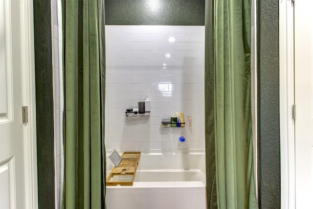 bathroom with a washtub, curtained shower, and a textured wall