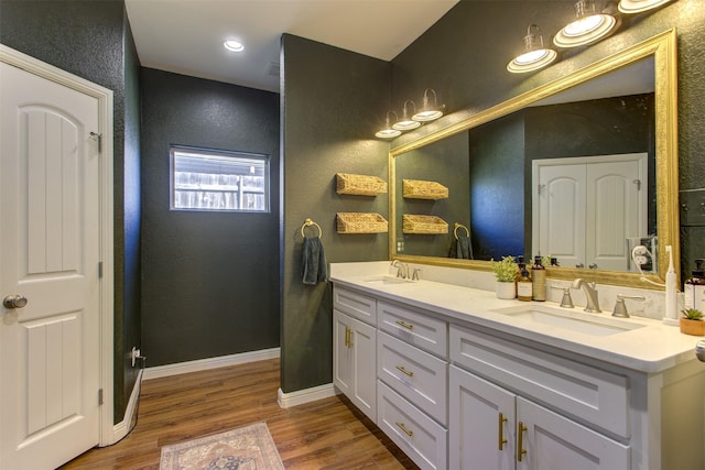 full bathroom with double vanity, a sink, baseboards, and wood finished floors