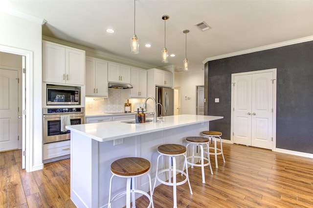 kitchen featuring crown molding, stainless steel appliances, visible vents, a sink, and under cabinet range hood