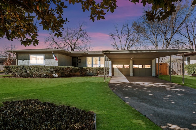 view of front of property with aphalt driveway, brick siding, fence, a carport, and a front lawn