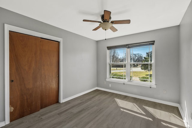 unfurnished bedroom featuring a ceiling fan, a closet, baseboards, and wood finished floors