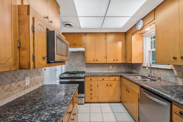 kitchen featuring light tile patterned floors, appliances with stainless steel finishes, a sink, under cabinet range hood, and backsplash