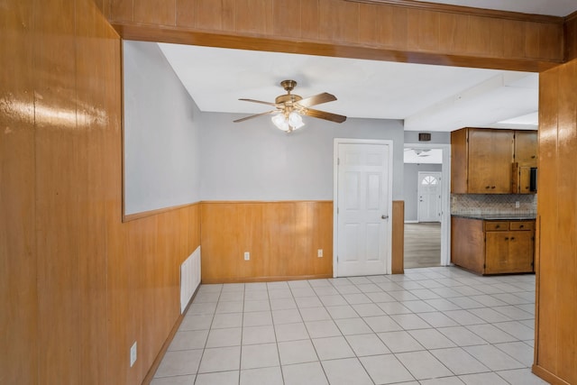 spare room featuring ceiling fan, light tile patterned floors, a wainscoted wall, wood walls, and visible vents