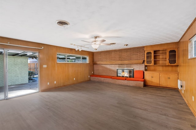 unfurnished living room featuring a fireplace, visible vents, a ceiling fan, wooden walls, and wood finished floors