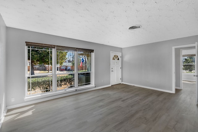 spare room with visible vents, a textured ceiling, baseboards, and wood finished floors