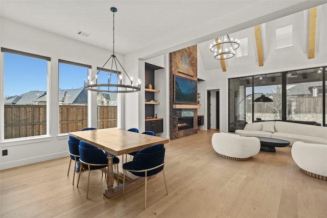 dining room with an inviting chandelier, light wood-style flooring, a fireplace, and built in shelves