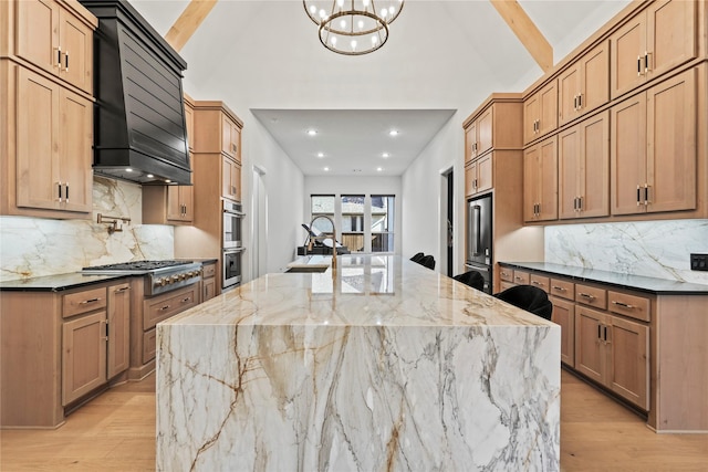 kitchen with dark stone counters, light wood-style flooring, custom range hood, stainless steel appliances, and a sink