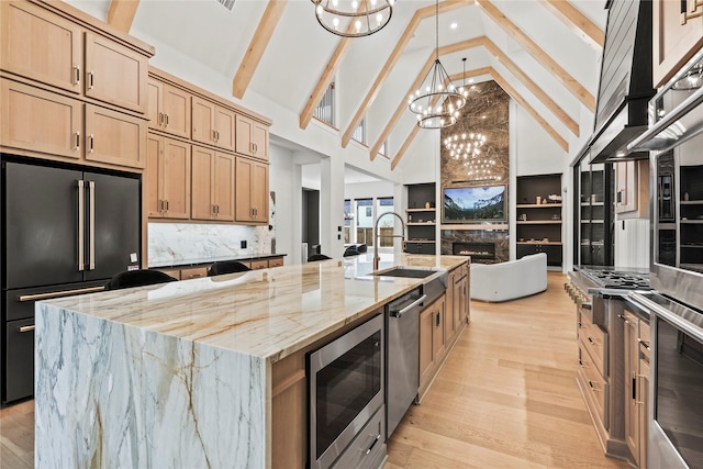 kitchen featuring light stone counters, a sink, a lit fireplace, appliances with stainless steel finishes, and light wood finished floors