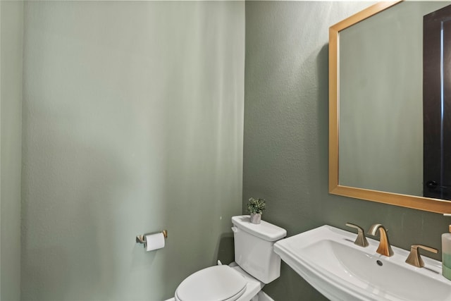 half bath with a textured wall, a sink, and toilet