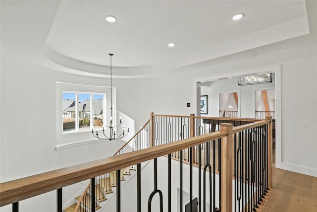 hall with baseboards, wood finished floors, a tray ceiling, a chandelier, and recessed lighting