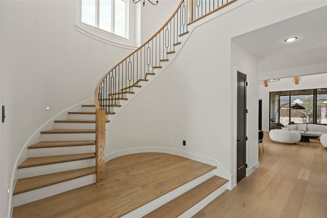 stairs with recessed lighting, baseboards, a high ceiling, and wood finished floors