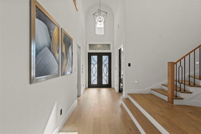 entryway with baseboards, wood-type flooring, stairway, a high ceiling, and a notable chandelier