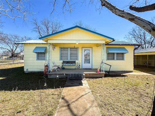 bungalow-style home featuring covered porch, metal roof, and a front lawn