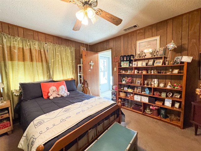 bedroom featuring a textured ceiling, wood walls, carpet flooring, visible vents, and a ceiling fan