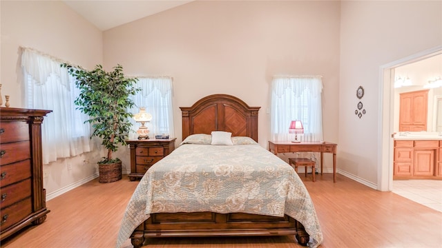 bedroom featuring baseboards, high vaulted ceiling, ensuite bath, and light wood-style floors