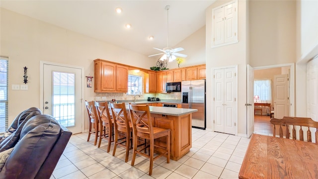 kitchen with black microwave, light tile patterned floors, stainless steel refrigerator with ice dispenser, and a kitchen bar