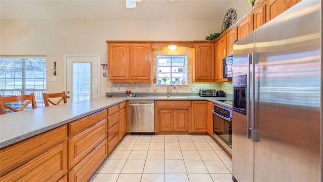 kitchen with light tile patterned floors, stainless steel appliances, tasteful backsplash, light countertops, and a sink