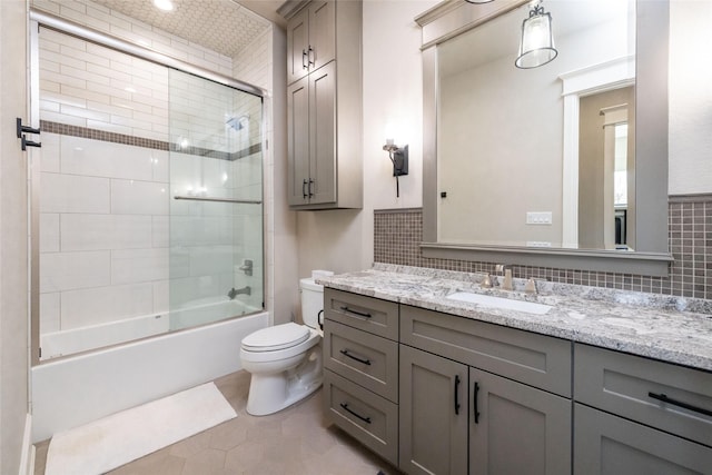 bathroom featuring toilet, shower / bath combination with glass door, vanity, backsplash, and tile patterned floors