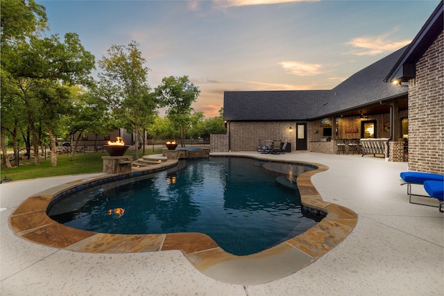 pool at dusk featuring a patio area and a pool with connected hot tub