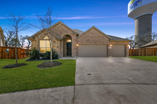 view of front facade with brick siding, a lawn, an attached garage, fence, and driveway