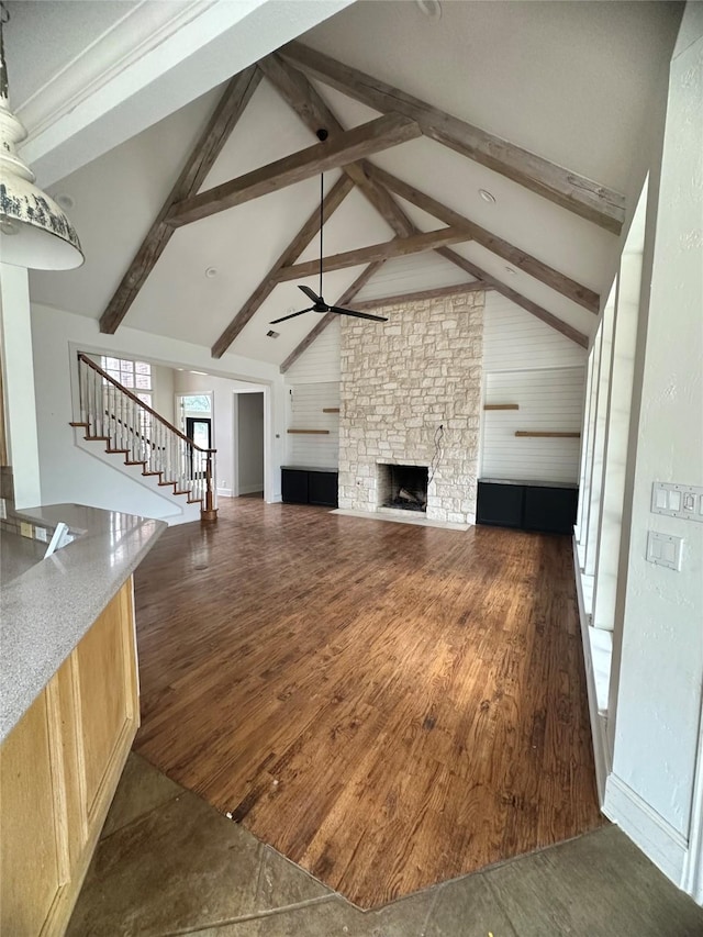 unfurnished living room with stairs, beam ceiling, dark wood-type flooring, and a stone fireplace