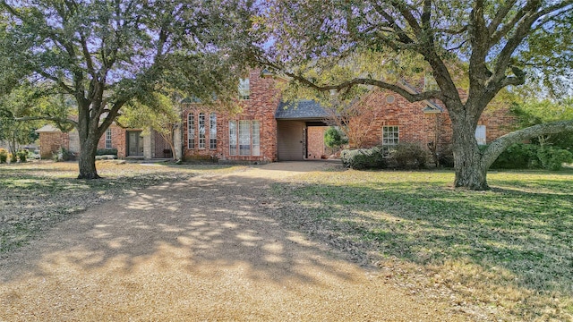 view of property hidden behind natural elements featuring driveway, a front yard, and brick siding