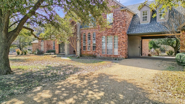 view of front facade with brick siding, dirt driveway, and roof with shingles