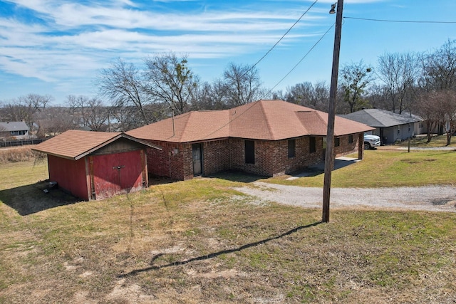 view of front facade featuring an outbuilding, a storage shed, brick siding, driveway, and a front yard