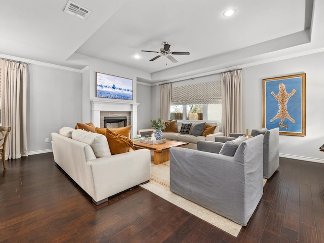 living area with dark wood-style flooring, a fireplace, visible vents, baseboards, and a tray ceiling