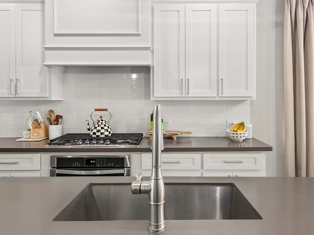 kitchen with appliances with stainless steel finishes, dark countertops, a sink, and white cabinets