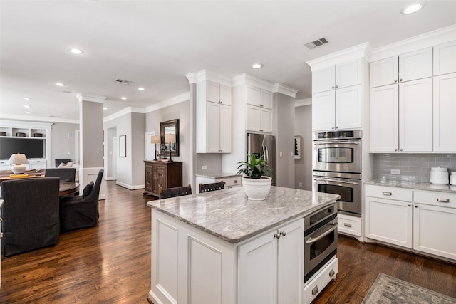 kitchen with stainless steel appliances, white cabinetry, visible vents, open floor plan, and ornate columns