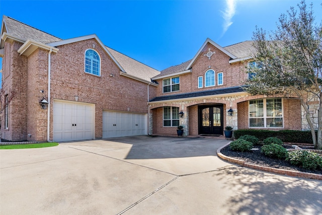 traditional-style house with french doors, brick siding, an attached garage, and concrete driveway