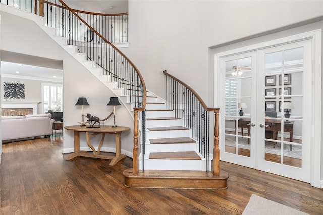 staircase featuring french doors, wood finished floors, a high ceiling, and baseboards