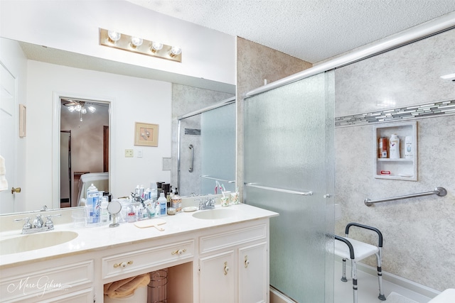 full bathroom with double vanity, a shower stall, a textured ceiling, and a sink