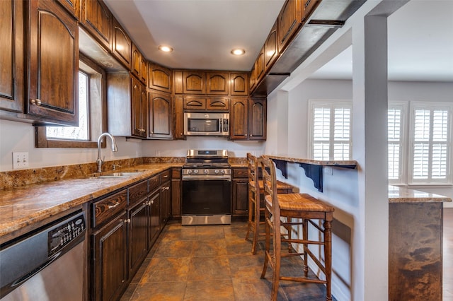 kitchen with stone countertops, recessed lighting, a sink, a kitchen breakfast bar, and appliances with stainless steel finishes