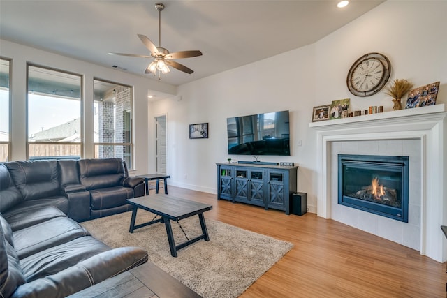 living room featuring wood finished floors, visible vents, baseboards, a ceiling fan, and a tiled fireplace