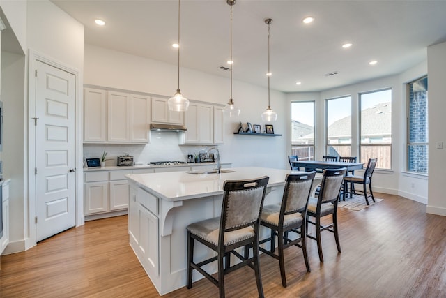 kitchen with a sink, gas stovetop, light countertops, light wood-type flooring, and backsplash