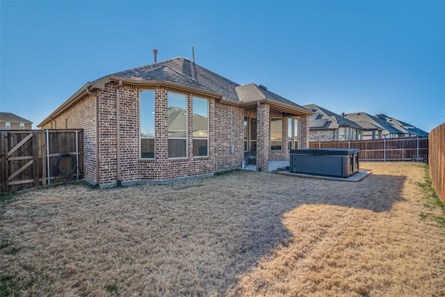 back of house with brick siding, a yard, a hot tub, and a fenced backyard