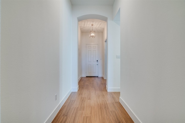 corridor featuring arched walkways, light wood-style floors, and baseboards