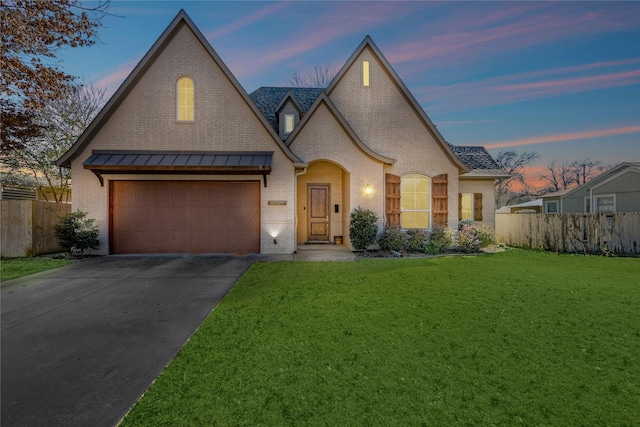 french country style house featuring a yard, fence, brick siding, and driveway