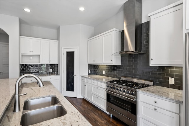 kitchen featuring white cabinets, stainless steel range, wall chimney range hood, and a sink