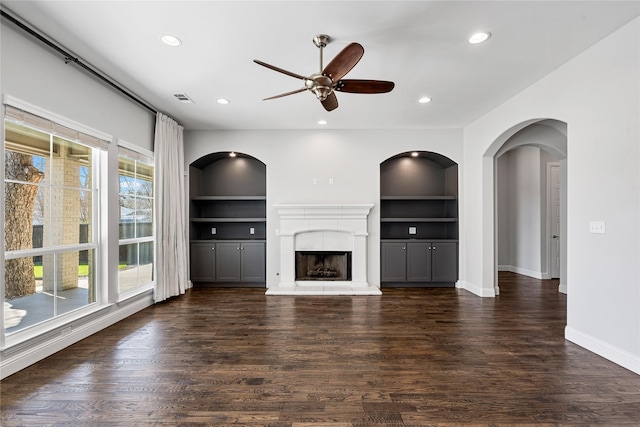 unfurnished living room featuring a fireplace with raised hearth, recessed lighting, wood finished floors, baseboards, and built in features