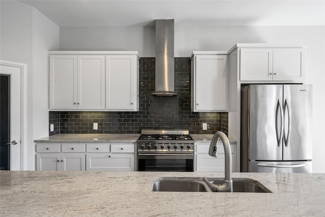 kitchen featuring stainless steel appliances, a sink, white cabinetry, wall chimney range hood, and decorative backsplash