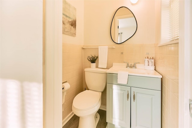 bathroom with toilet, a wainscoted wall, tile walls, and vanity