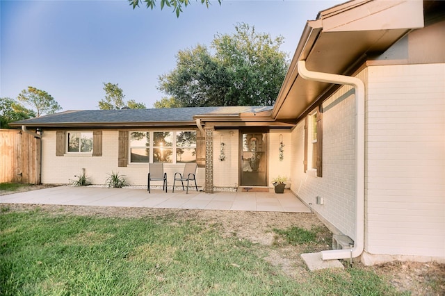 exterior space with roof with shingles, a yard, brick siding, a patio, and fence