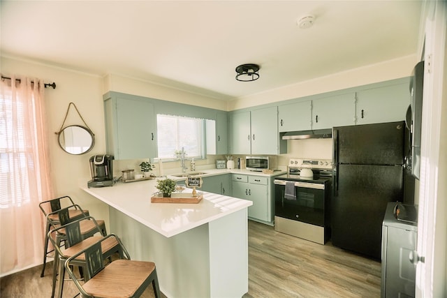 kitchen with appliances with stainless steel finishes, light wood-style floors, a peninsula, green cabinetry, and under cabinet range hood