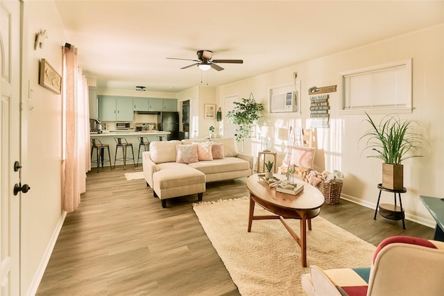 living room with ceiling fan, a wall mounted AC, light wood-type flooring, and baseboards