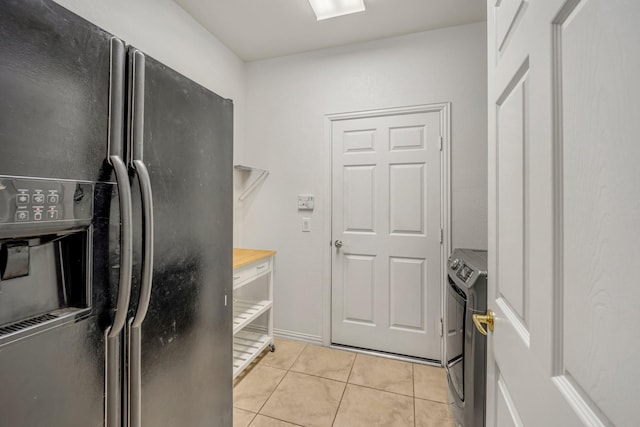 kitchen featuring light tile patterned floors, light countertops, black fridge, and washer / dryer