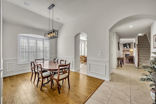 dining space featuring arched walkways, lofted ceiling, a fireplace, light wood-style floors, and stairs