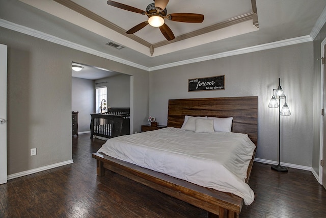 bedroom featuring a tray ceiling, visible vents, baseboards, and wood finished floors